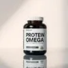 A sleek and modern protein supplement bottle, showcasing the "Protein Omega" label in a clean, minimalist design. The bottle is positioned on a reflective, glass-like surface, casting a subtle shadow below. Soft, directional lighting illuminates the supplement from the side, creating a sense of depth and dimension. The overall scene has a professional, high-quality aesthetic, inviting the viewer to imagine the premium quality of the product. The background is a simple, neutral color that allows the supplement bottle to be the focal point, drawing the eye to the key details and branding.